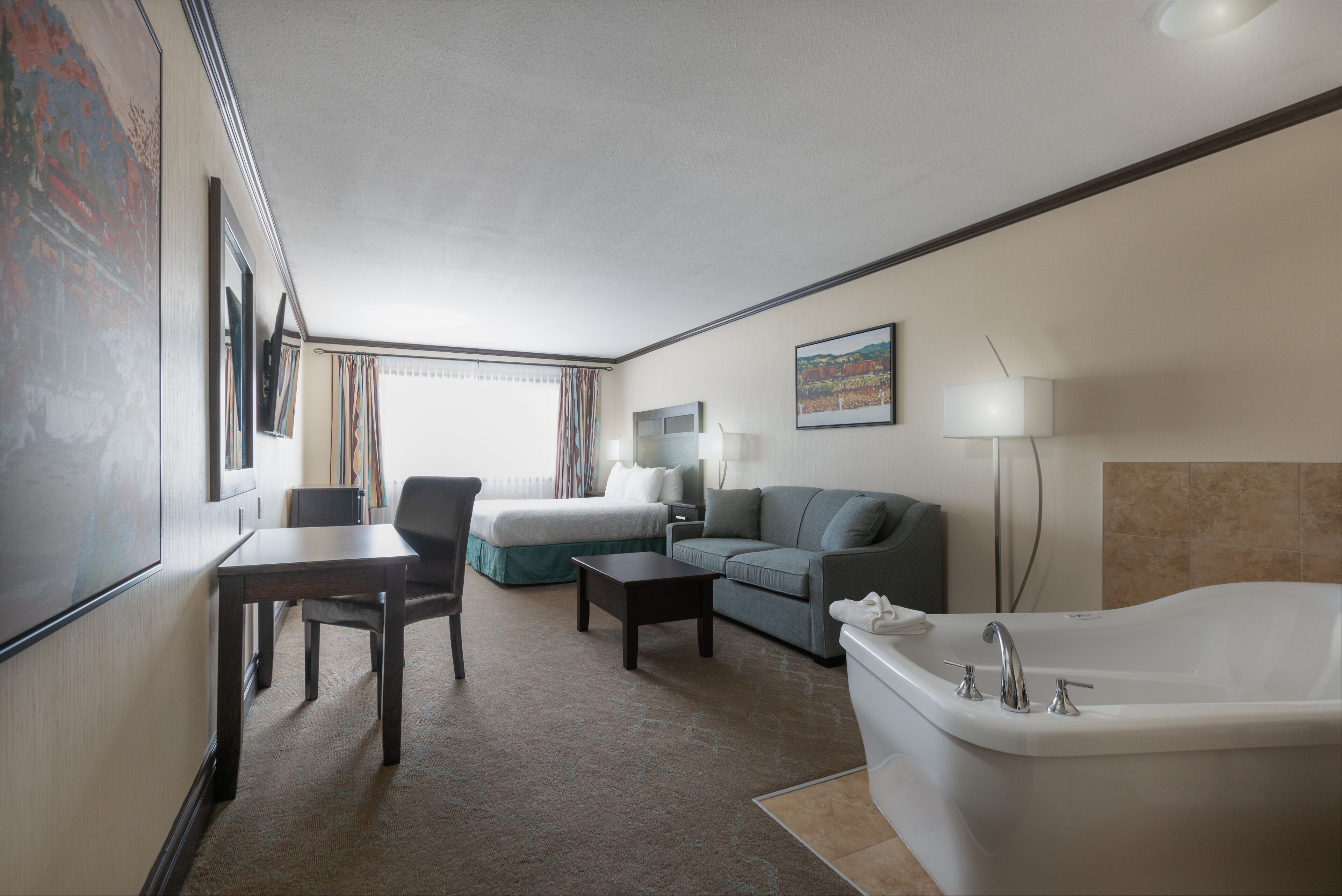 A hotel room with a bed, a sofa, a desk, a chair, a lamp, and a bathtub.
