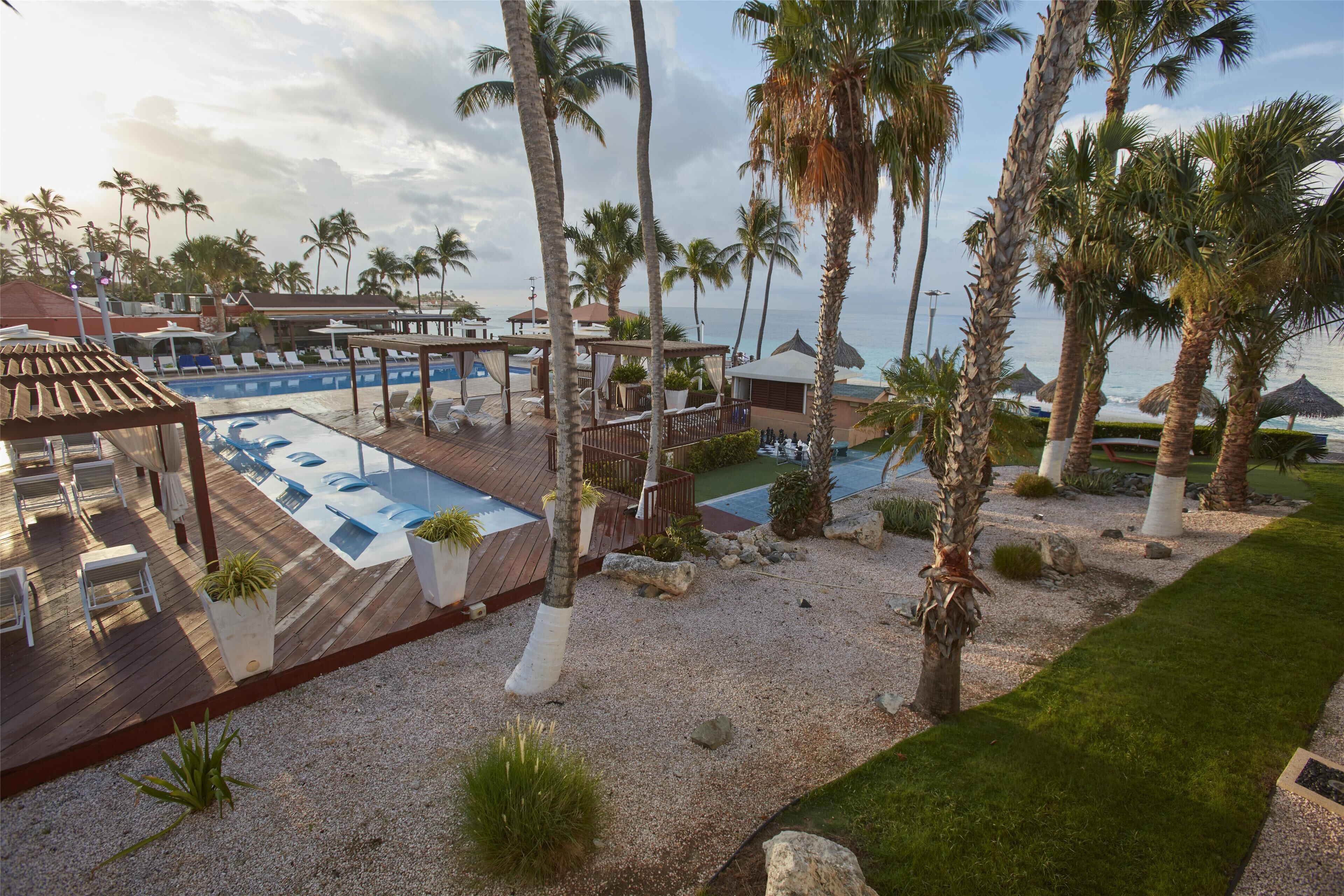 Ein Resort mit Poolbereich, Palmen und Blick auf den Ozean.
