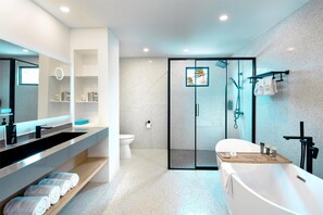 A modern bathroom with a freestanding bathtub, a glass-enclosed shower, and a vanity with a large mirror and shelves.