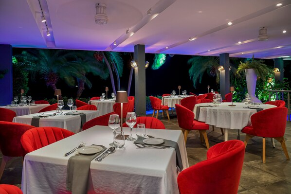 A restaurant with tables set for dining, red chairs, and a tropical mural on the wall.