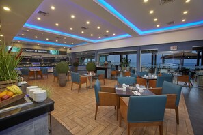 A modern restaurant with a variety of seating options, including tables and chairs, and a buffet area with fruits and dishes.