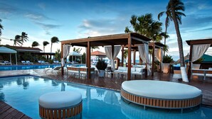 A pool area with lounge chairs, a wooden deck, and a covered seating area with curtains.
