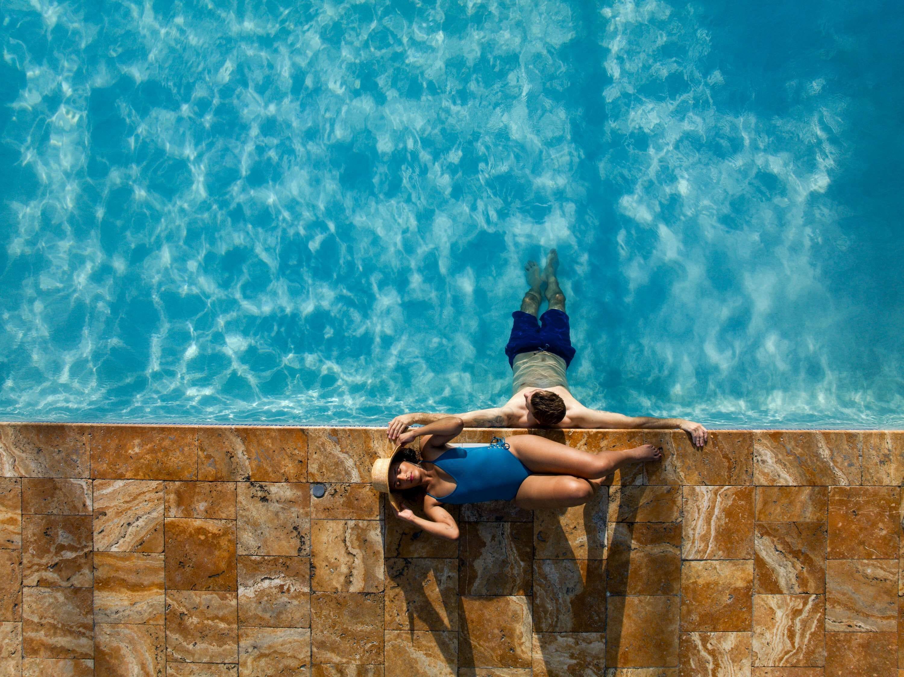 Una persona recostada al borde de una piscina con baldosas, con vista despejada al agua.