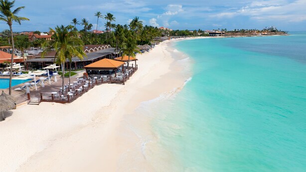 A beach resort with a pool, lounge chairs, and a restaurant with a view of the ocean.