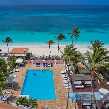 A resort with a swimming pool, beach, and palm trees.