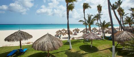 A beach with thatched umbrellas, palm trees, and a clear blue sky.
