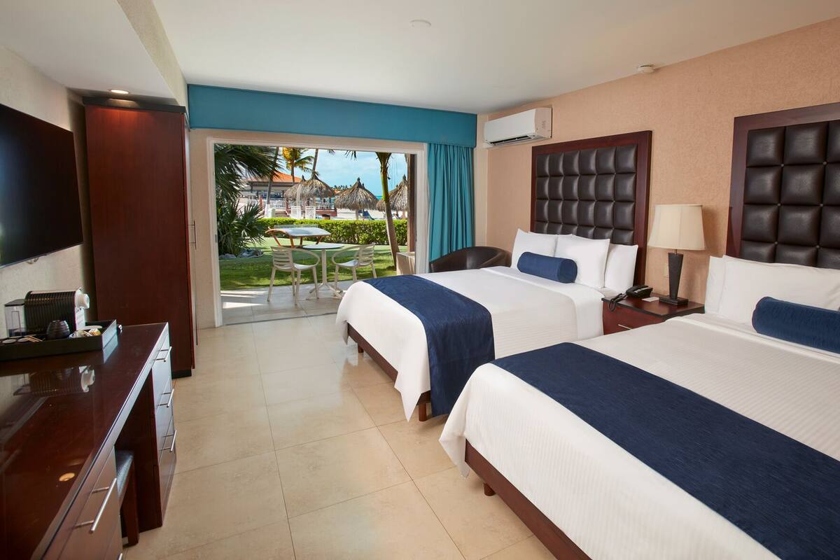 A hotel room with two beds, a TV, a desk, and a view of a pool and resort.