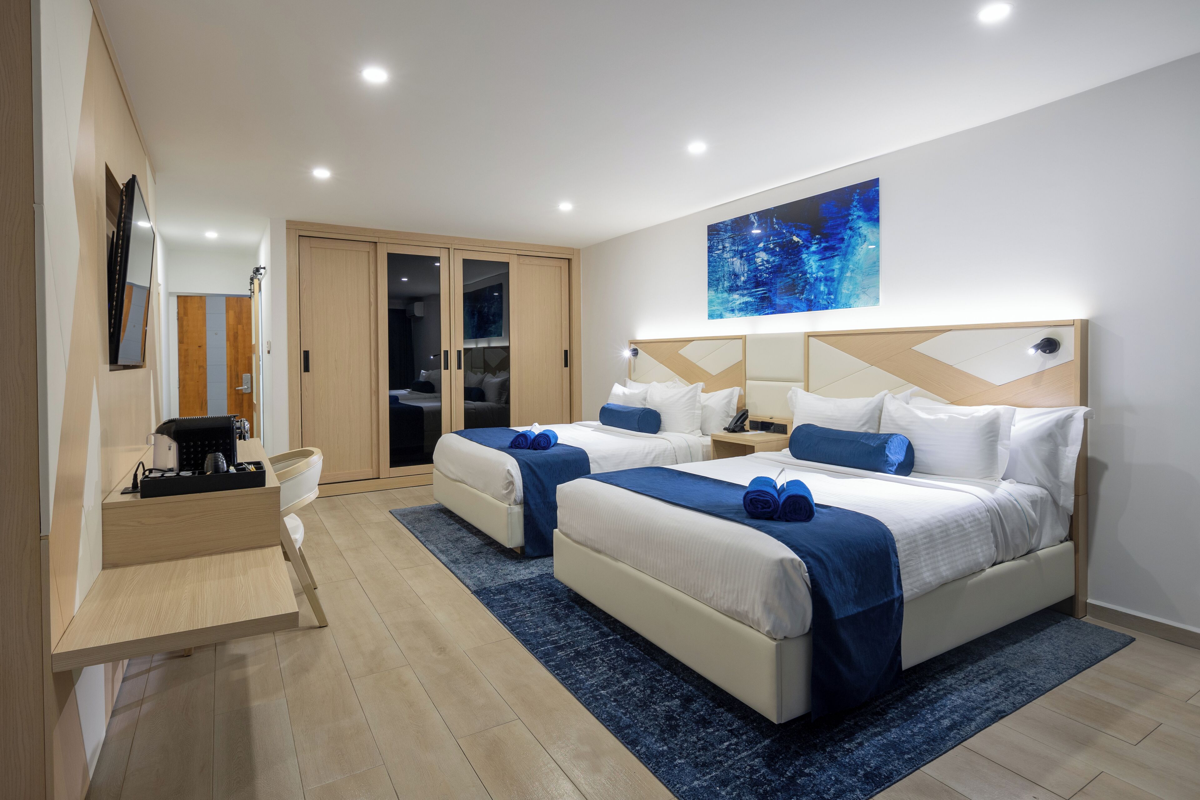 A modern hotel room with two beds, a desk, and a large window.