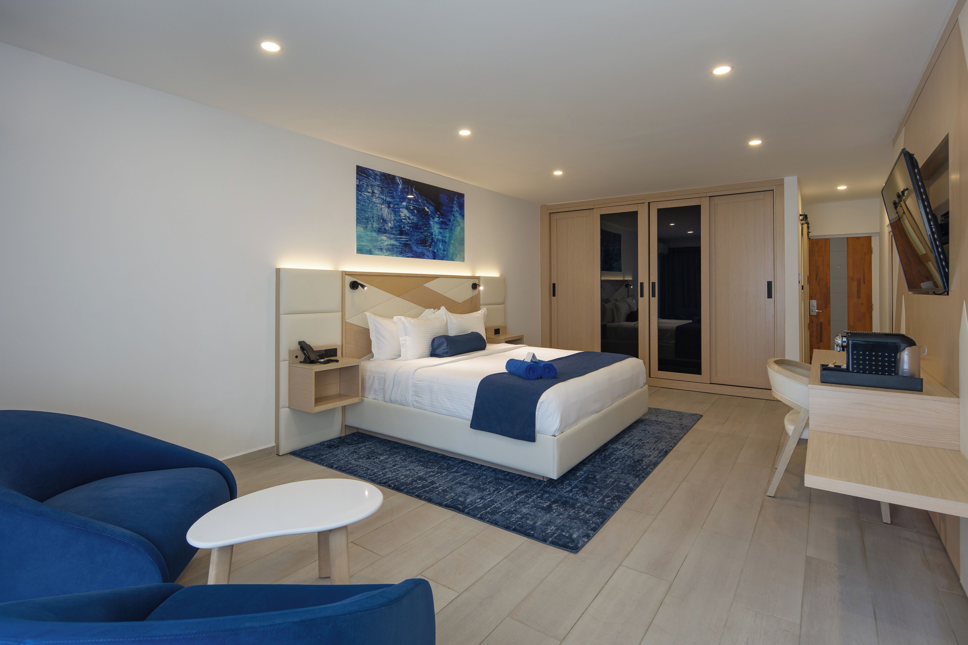 Habitación de hotel moderna con una cama grande, un escritorio, un sofá azul y un cuadro en la pared.