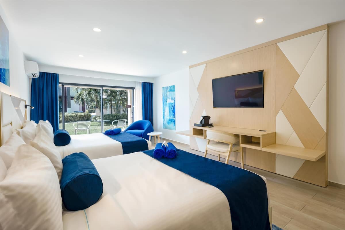 A modern hotel room with two beds, a desk, a TV, and a view of the outdoors.