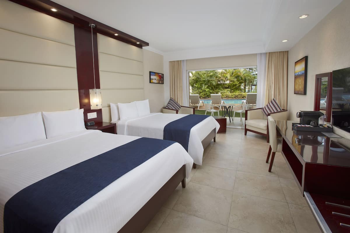 A hotel room with two beds, a desk, a chair, a TV, and a view of the outdoors.