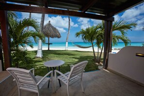 A covered outdoor seating area with a view of a beach and palm trees.