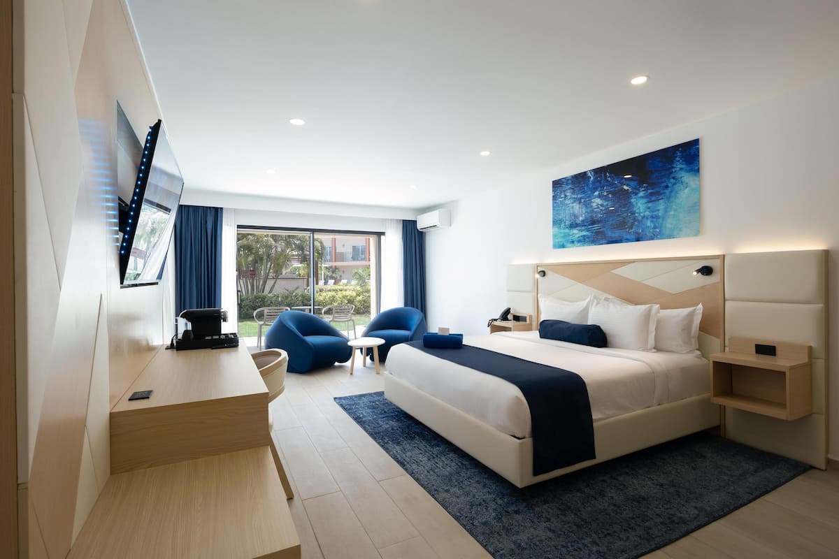 A modern hotel room with a large bed, a desk, and a chair. There is a window with a view of the outside.
