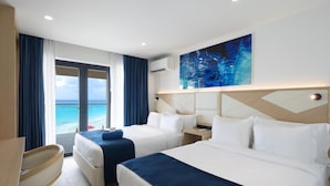 A hotel room with two beds, a desk, and a view of the ocean.