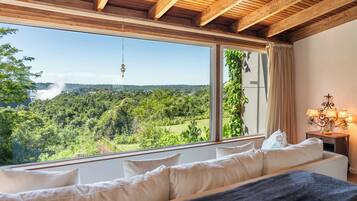 Une chambre dotée d’une grande fenêtre donnant sur un paysage luxuriant et une cascade.