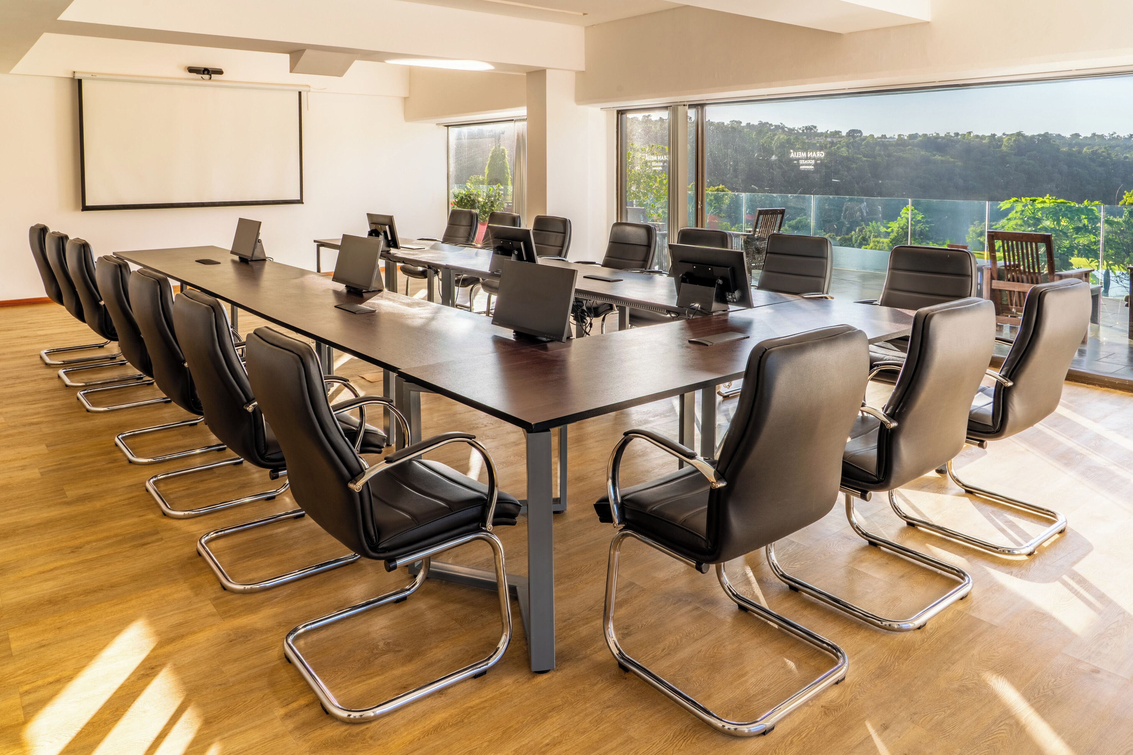 A conference room with a long table, multiple chairs, laptops, and a projector screen.