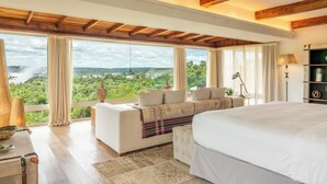 Un dormitorio amplio con una cama grande, un sofá y vistas a un paisaje exuberante a través de amplios ventanales.