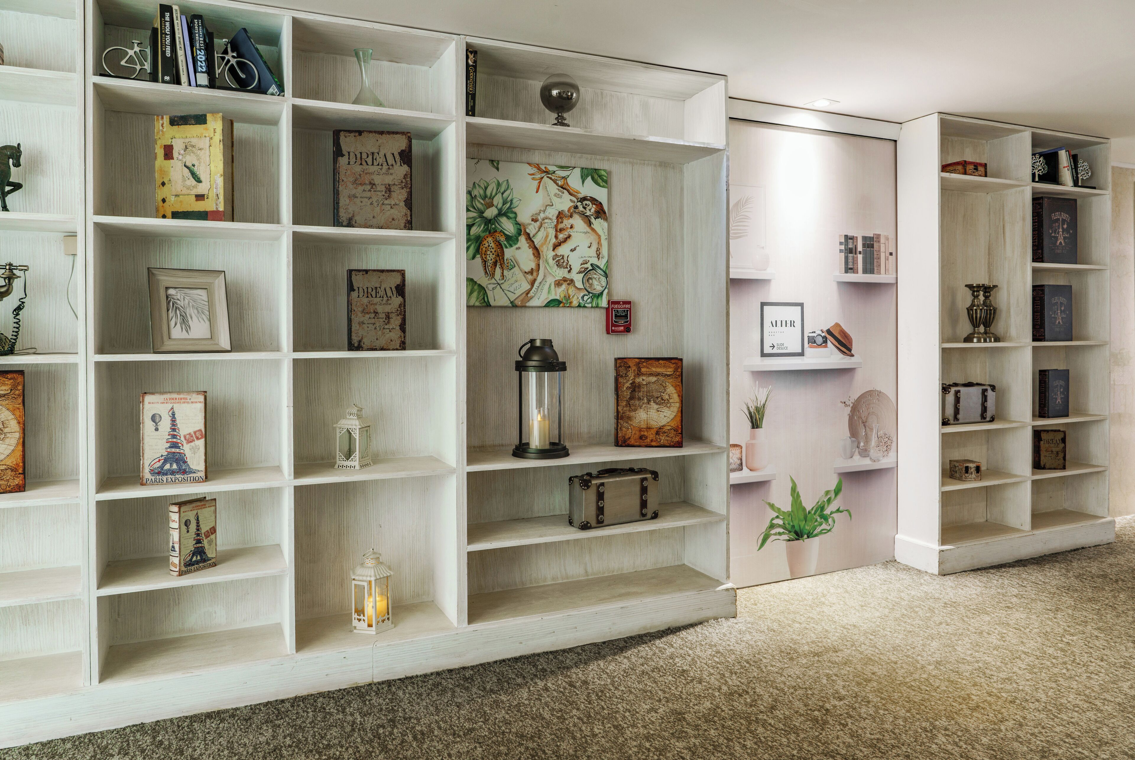 A library with multiple shelves containing books, decorative items, and a map.