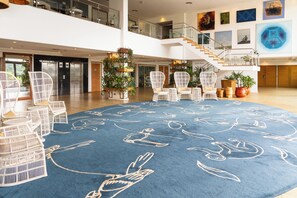 A spacious lobby with a blue carpet featuring white animal illustrations, white wicker chairs, and a staircase leading to an upper level.