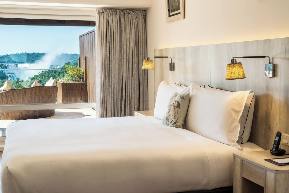A hotel room with a large bed, two bedside lamps, a nightstand with a phone, and a view of a waterfall.