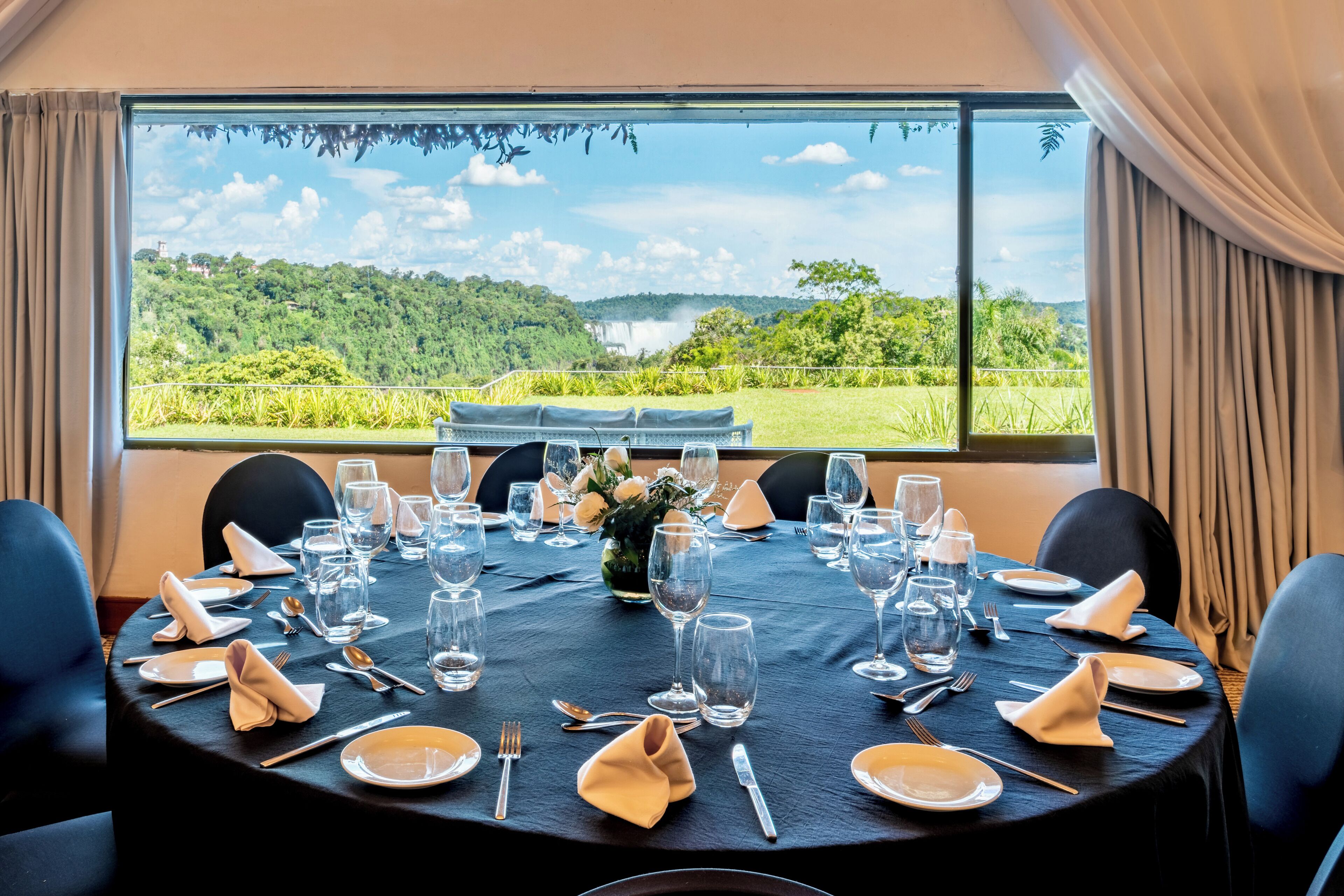 A dining table set for a meal with a view of a lush landscape and waterfall.