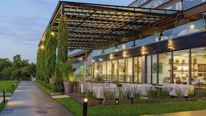 Een modern gebouw met een overdekt terras, glazen wanden en een verzorgde tuin.