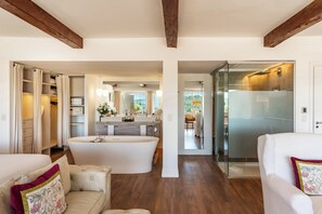 A spacious living area with a large white bathtub, a white sofa, and a glass-enclosed shower area.