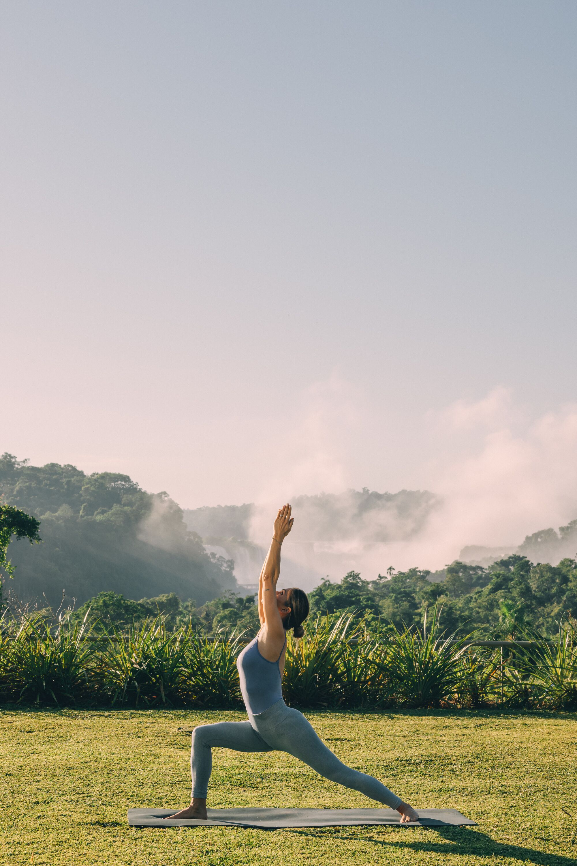 A person performing a yoga pose on a mat in a grassy area with a misty forest background.