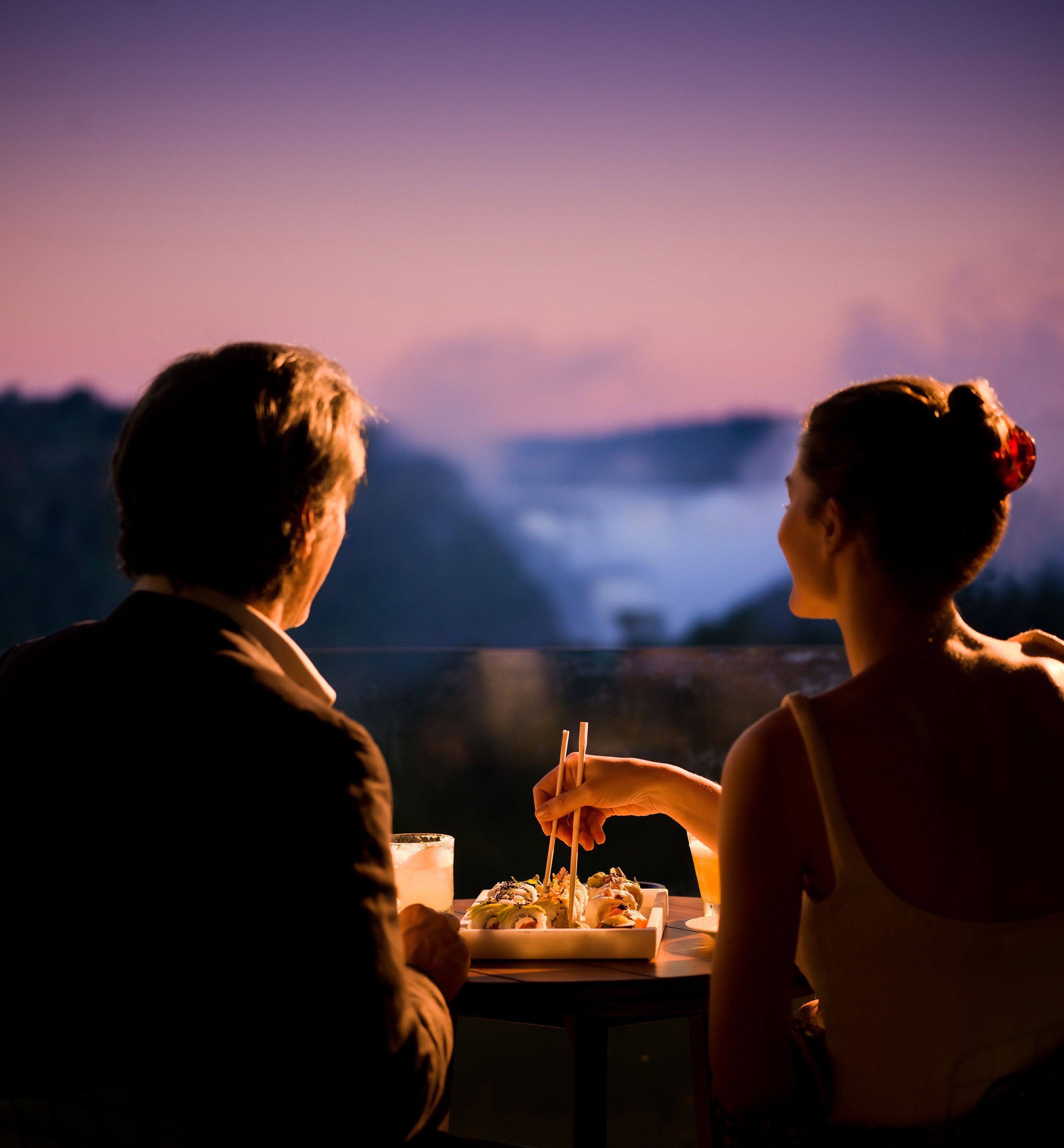 Duas pessoas jantando à mesa com vista para montanhas ao fundo.