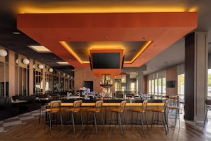 A bar area with a long counter, multiple stools, and a television screen.