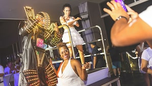 A person in a white dress standing on a platform with a railing, surrounded by people and a crowd. - Hotel Riu Palace Aruba - All Inclusive (Noord)