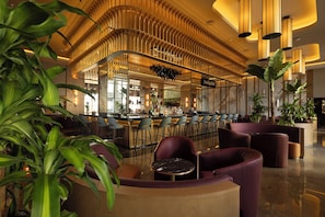 A modern bar area with a curved ceiling, bar stools, and a seating area with round tables. - Hotel Riu Palace Aruba - All Inclusive (Noord)
