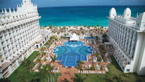A resort with a central pool, multiple balconies, and a view of the ocean. - Hotel Riu Palace Aruba - All Inclusive (Noord)