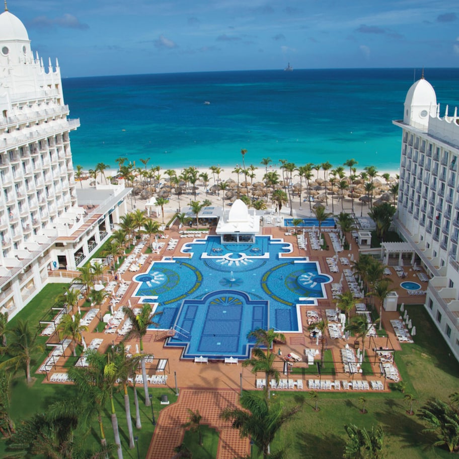 A resort with a central pool, multiple balconies, and a view of the ocean.