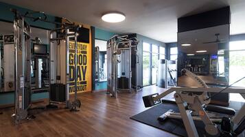 Ein Fitnessstudio mit verschiedenen Trainingsgeräten, einem motivierenden Spruch an der Wand und großen Fenstern für natürliches Licht.