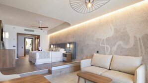 A modern hotel room with a bed, a sofa, a wooden coffee table, and a ceiling fan. - Hotel Riu Palace Aruba - All Inclusive (Noord)