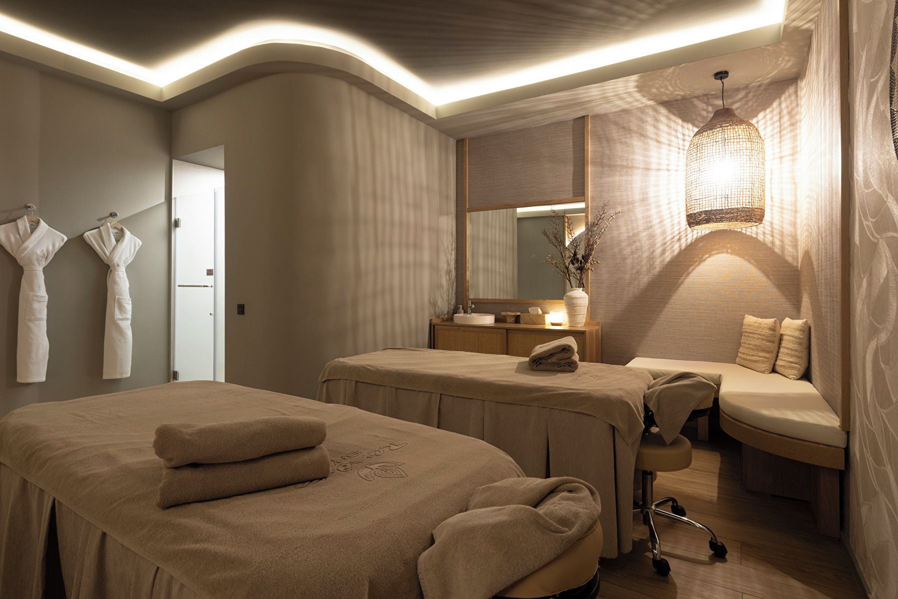Ein Spa-Raum mit zwei Massageliegen, einer Bank, einem Schminktisch mit Spiegel und einer Hängelampe.
