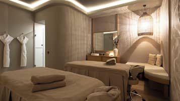 Ein Spa-Raum mit zwei Massageliegen, einer Bank, einem Schminktisch mit Spiegel und einer Hängelampe.