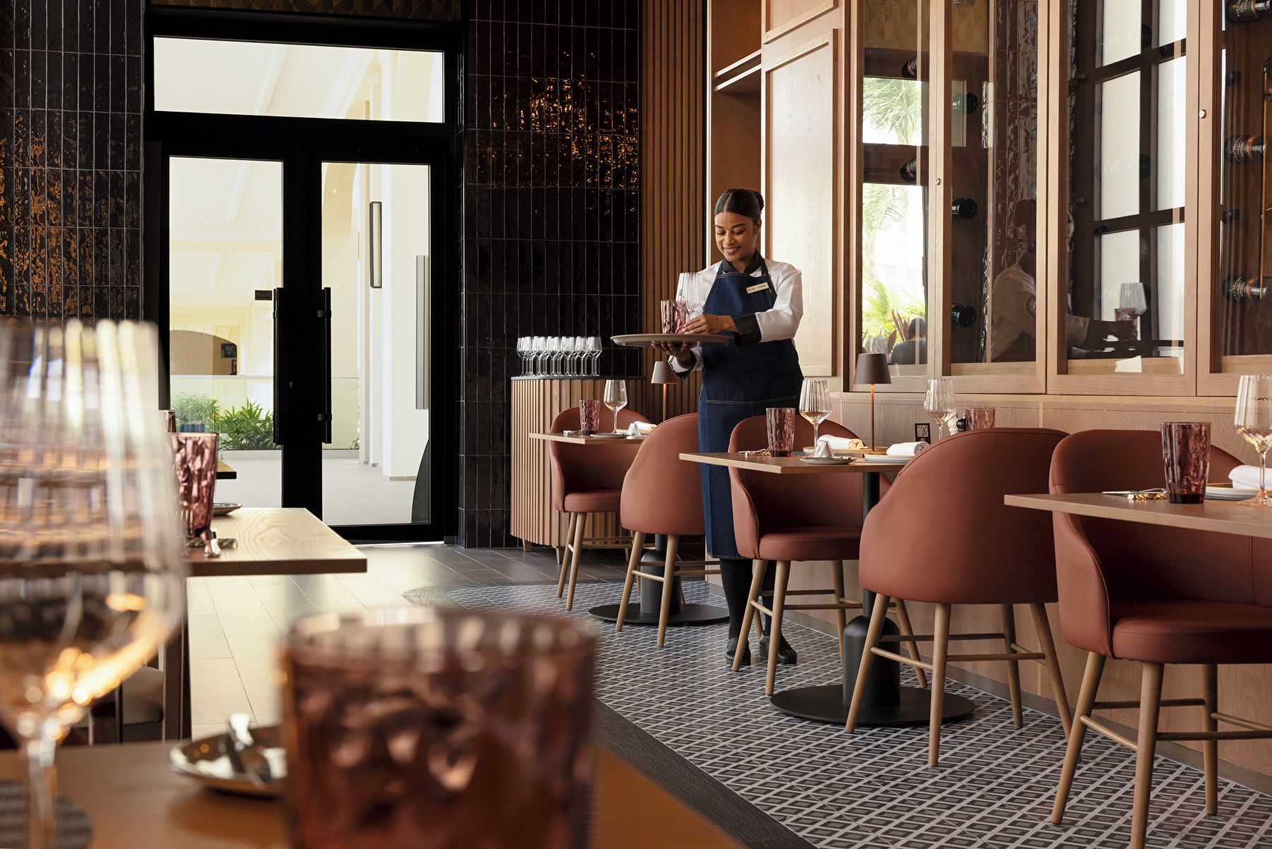 Ein Restaurantinneres mit Kellner im Service, Tischen mit Stühlen und Blick auf die Stadt durch die Fenster.