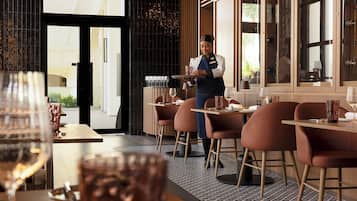 Ein Restaurantinneres mit Kellner im Service, Tischen mit Stühlen und Blick auf die Stadt durch die Fenster.