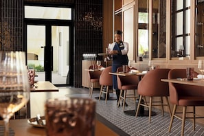 En restauranginteriör med en servitör som serverar, bord med stolar och utsikt över staden genom fönstren.