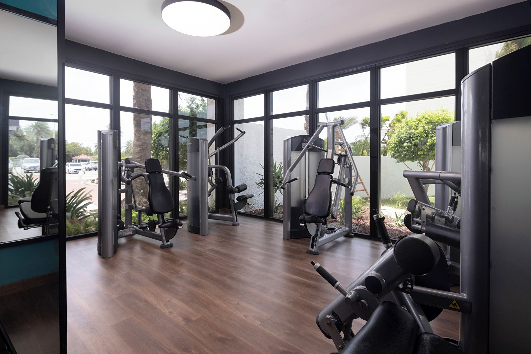 Un gimnasio con equipamiento de ejercicio, ventanas amplias y vistas al exterior.