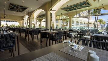 Un restaurant doté de nombreuses tables et chaises, de grandes fenêtres et offrant une vue sur un immeuble avec des balcons.