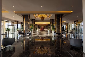 A modern lobby with a reflective floor, seating areas, and a central decorative feature. - Hotel Riu Palace Aruba - All Inclusive (Noord)