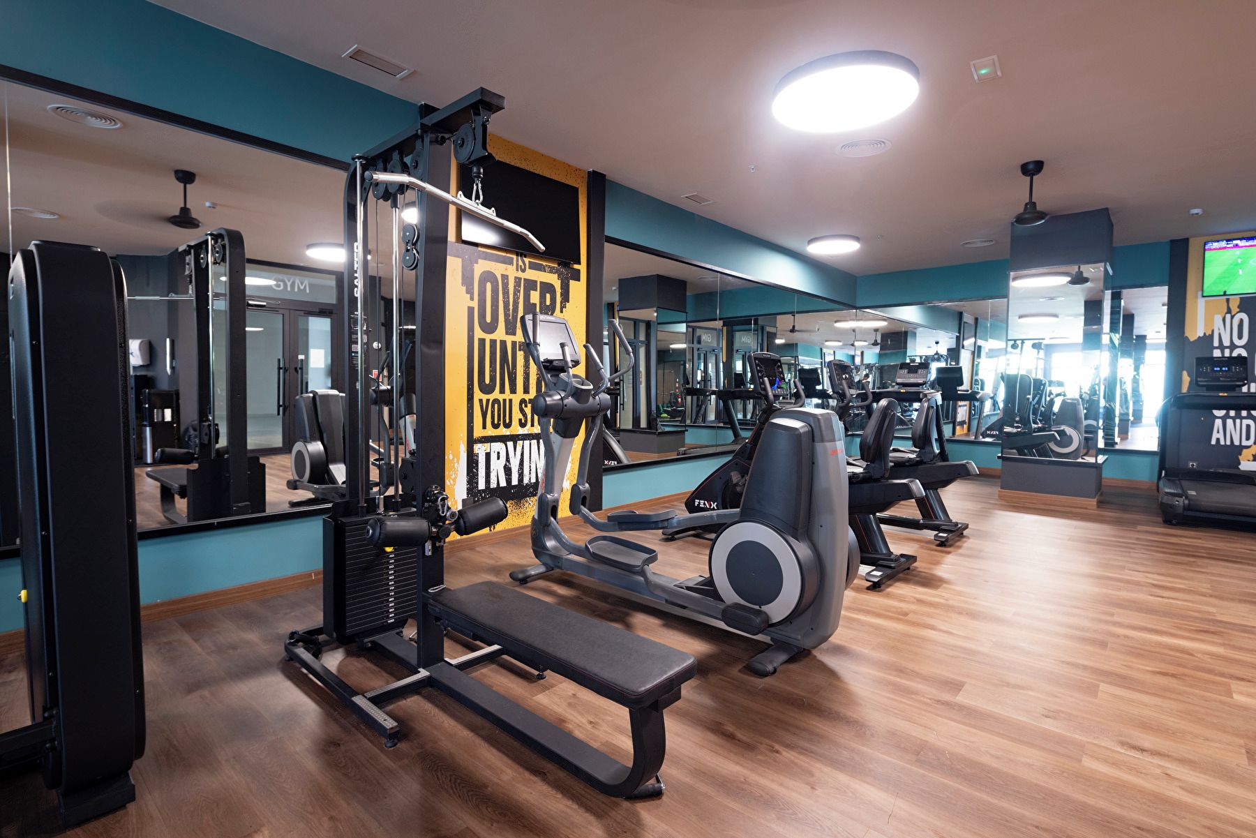 Ein Fitnessstudio mit Trainingsgeräten, Spiegeln und Holzboden.