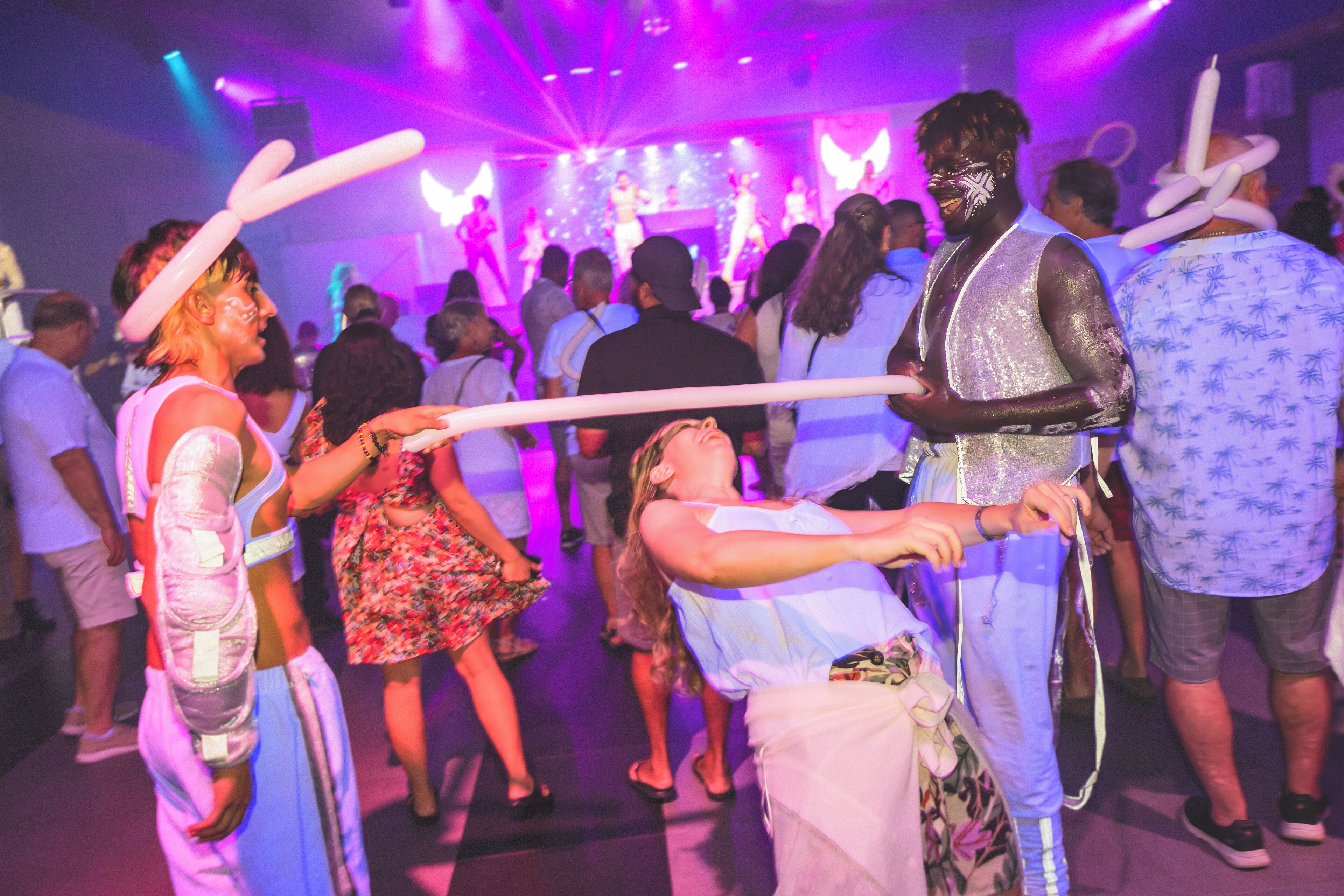 A crowded indoor event with people holding white balloons.