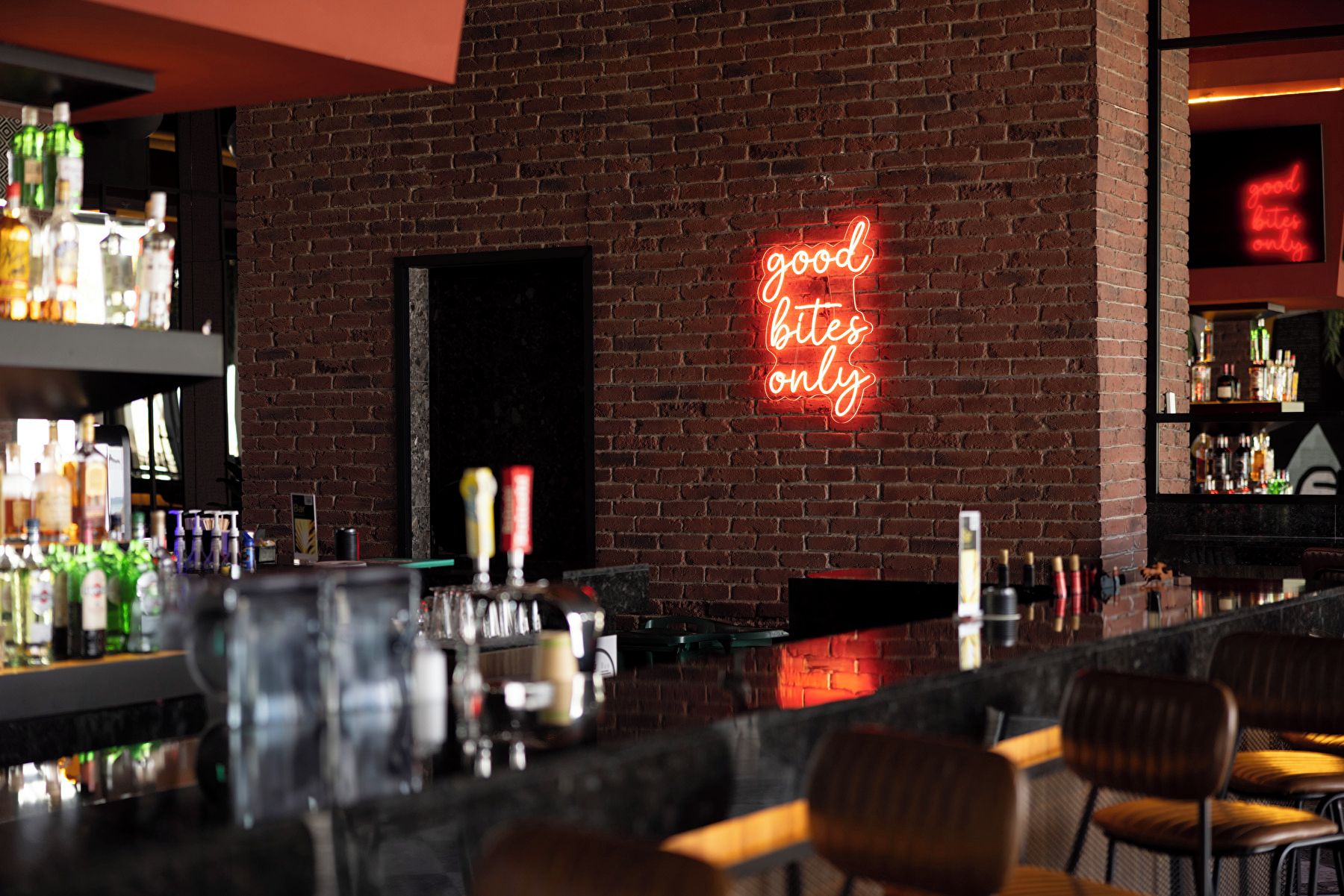 A bar area with a neon sign reading 'good bites only' and a brick wall.