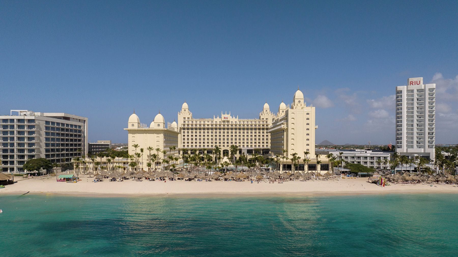 A large resort hotel with multiple buildings, a beach, and a clear blue sky.