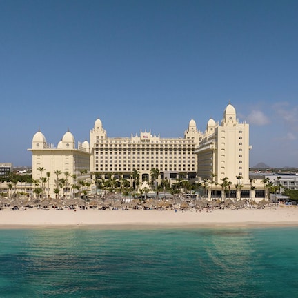 A large resort hotel with multiple buildings, a beach, and a clear blue sky.