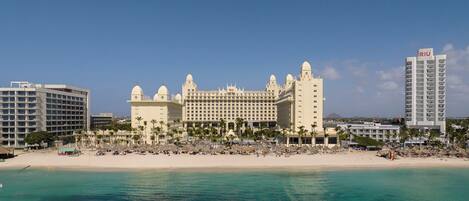 A large resort hotel with multiple buildings, a beach, and a clear blue sky.